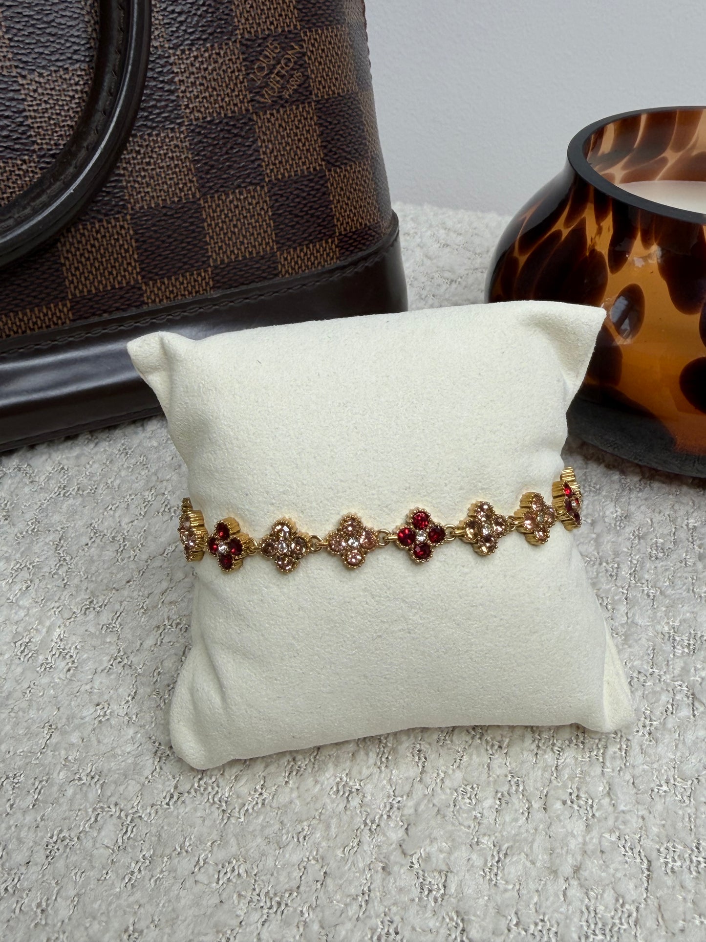 Bracelet en acier inoxydable doré orné de trèfles sertis de zircons rouges et cristaux brillants. Bijou résistant à l'eau et anti-allergique pour femme.
