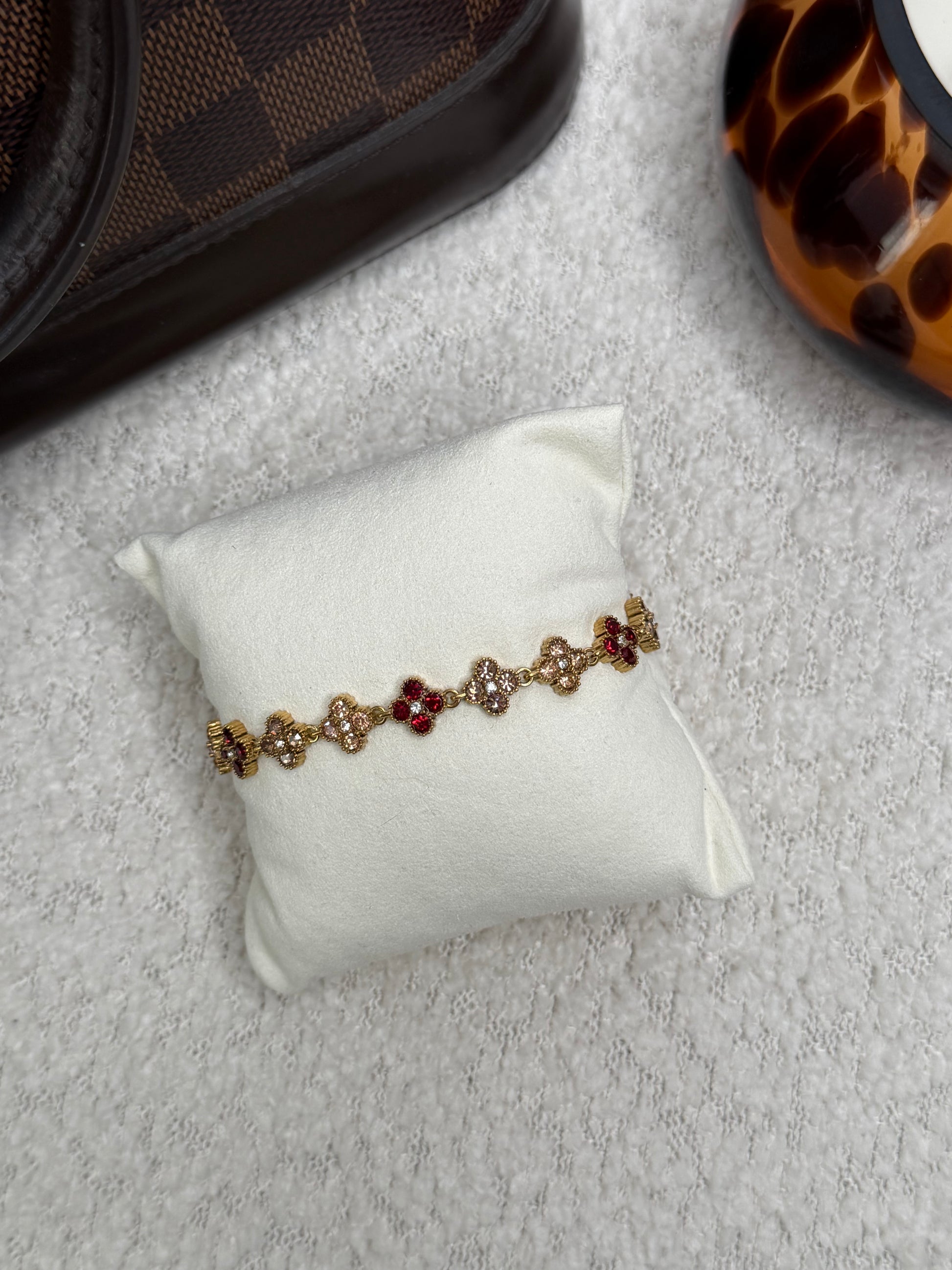 Bracelet en acier inoxydable doré orné de trèfles sertis de zircons rouges et cristaux brillants. Bijou résistant à l'eau et anti-allergique pour femme.
